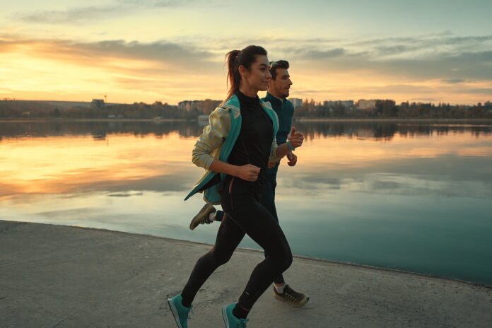 Young man and woman out for a run on the lake at the sunrise